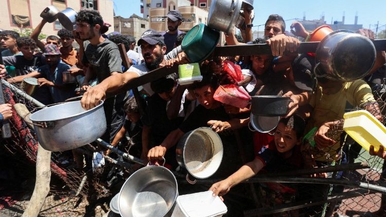 Civili palestinesi in fila per ricevere aiuti alimentari nella Striscia di Gaza, simbolo della fame usata come arma di guerra.